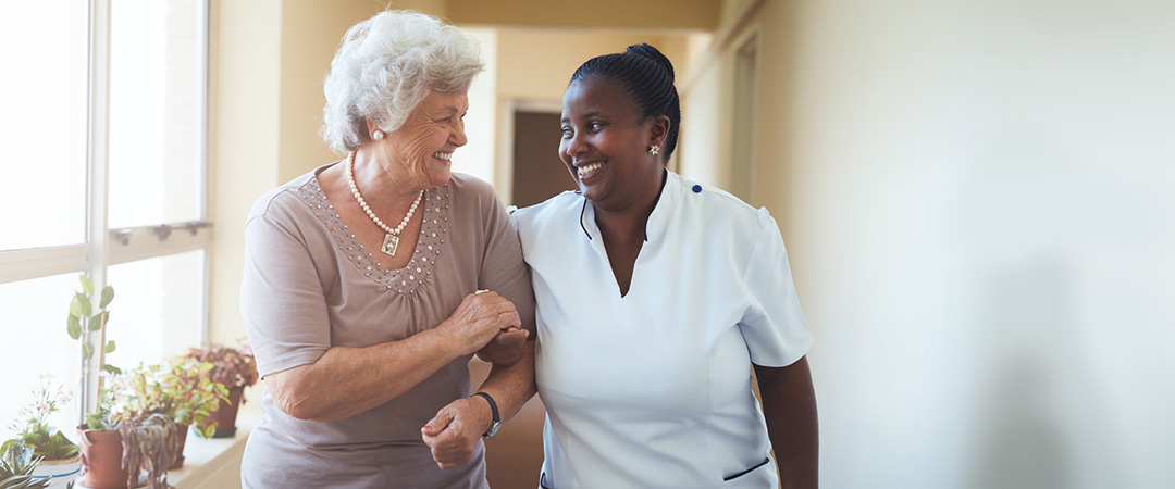 yolo-1080x450-10 Nurse and resident walking arm and arm down a bright hallway