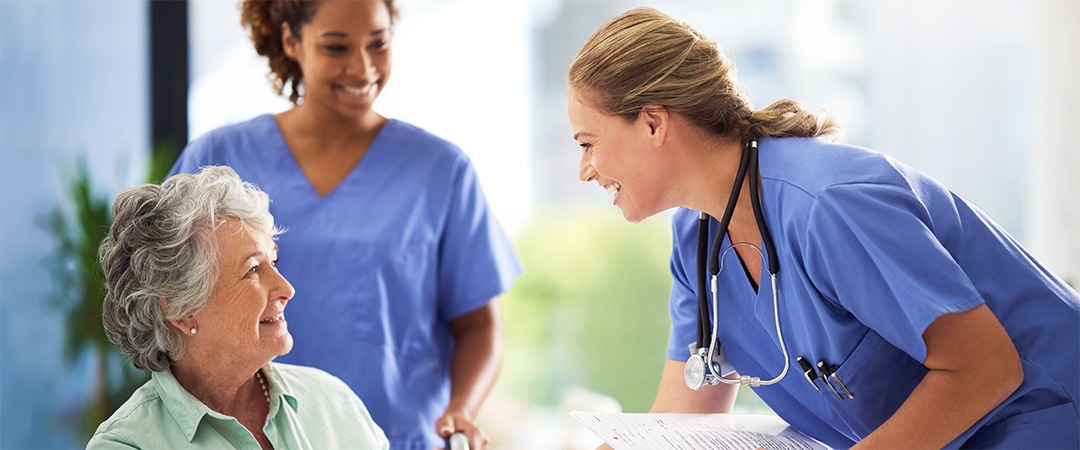 yolo-1080x450-102 Two female nurses smiling leaning down to welcome a new patient