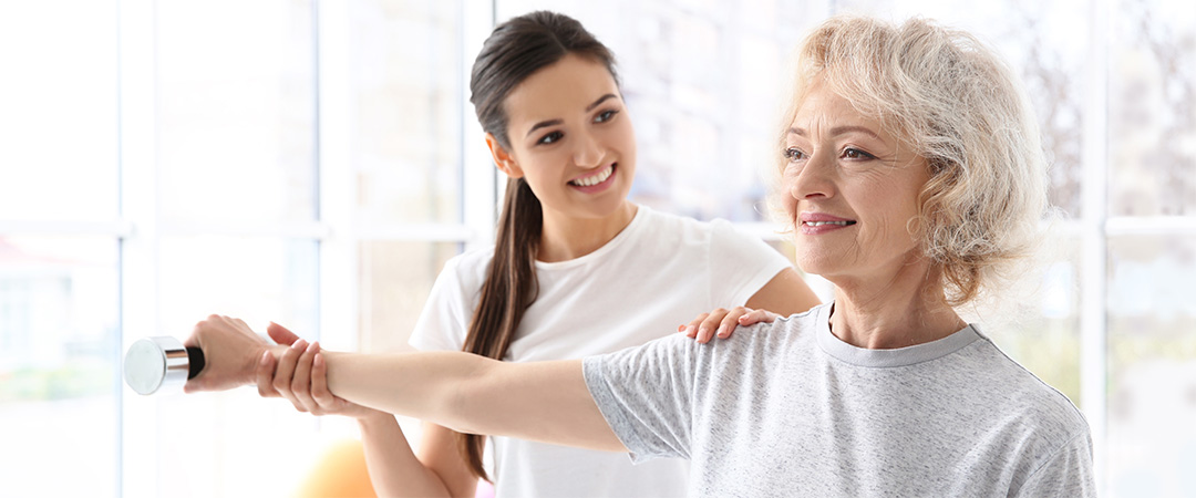 yolo-1080x450-30 Physical therapist holding a resident's shoulder and wrist assisting with weights