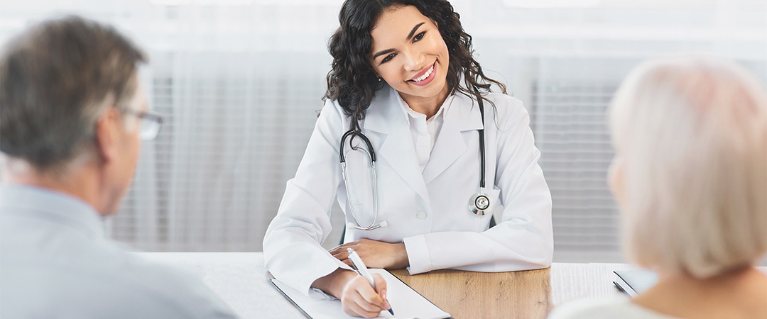 yolo-1080x450-55 Doctor with a stethoscope draped around her neck taking notes while speaking to a couple