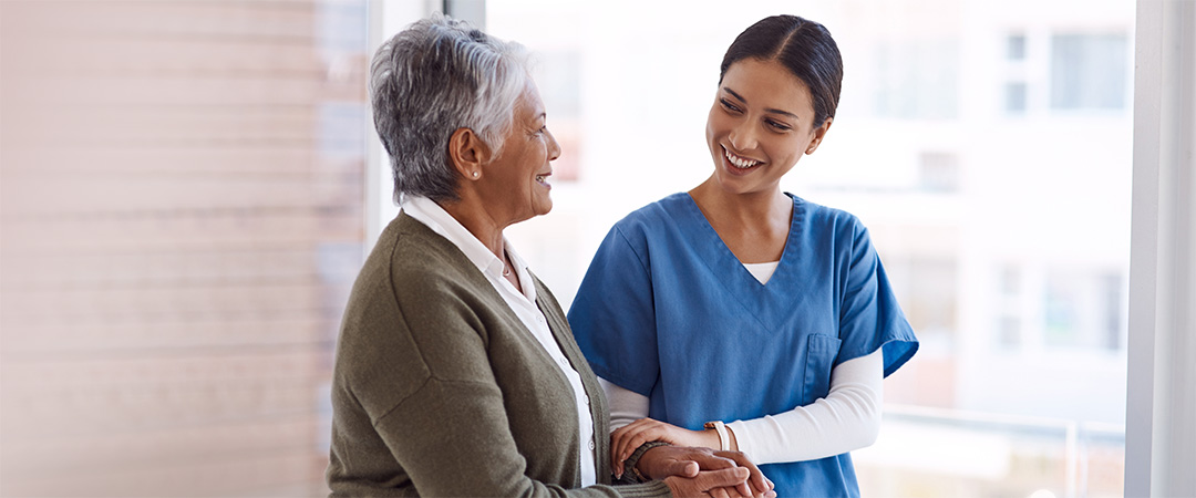 yolo-1080x450-95 Smiling female nurse walking arm in arm with an elderly female resident